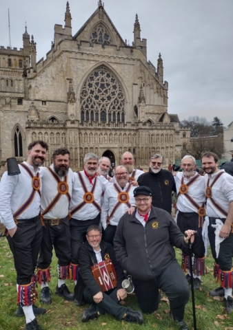 A photo of 11 Brighton Morris Men in front of Exeter Cathedral, at the start of the Inter-Varsity Folk Dance Festival